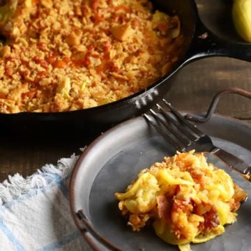 Southern Squash Casserole in a cast-iron skillet with a serving on a metal plate.