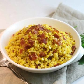 A white serving dish with fried corn topped with bacon.