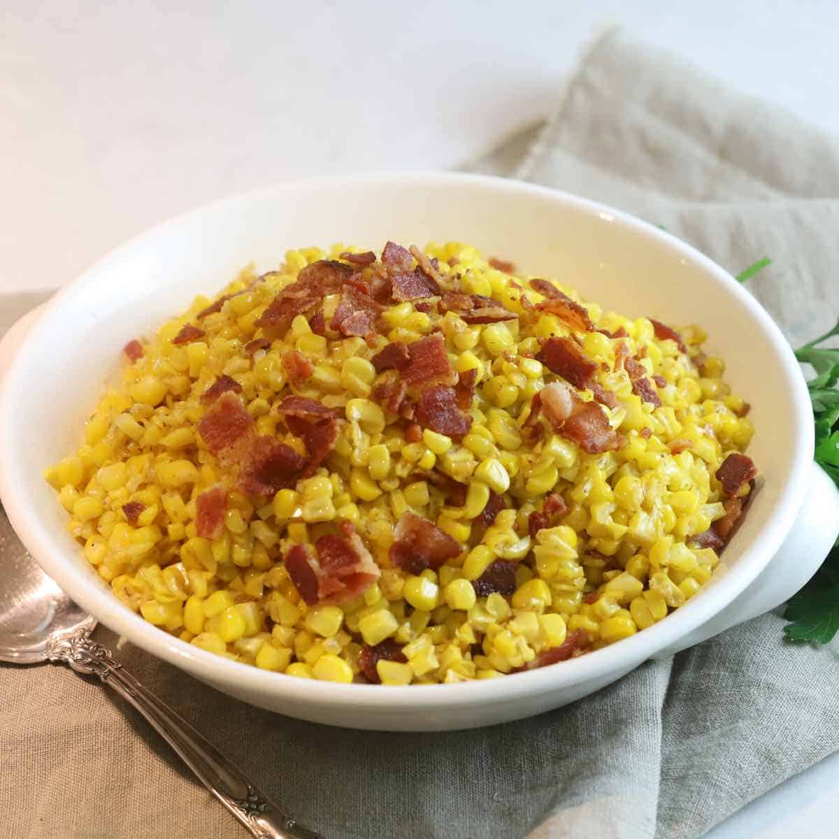 A white serving dish with fried corn topped with bacon. 