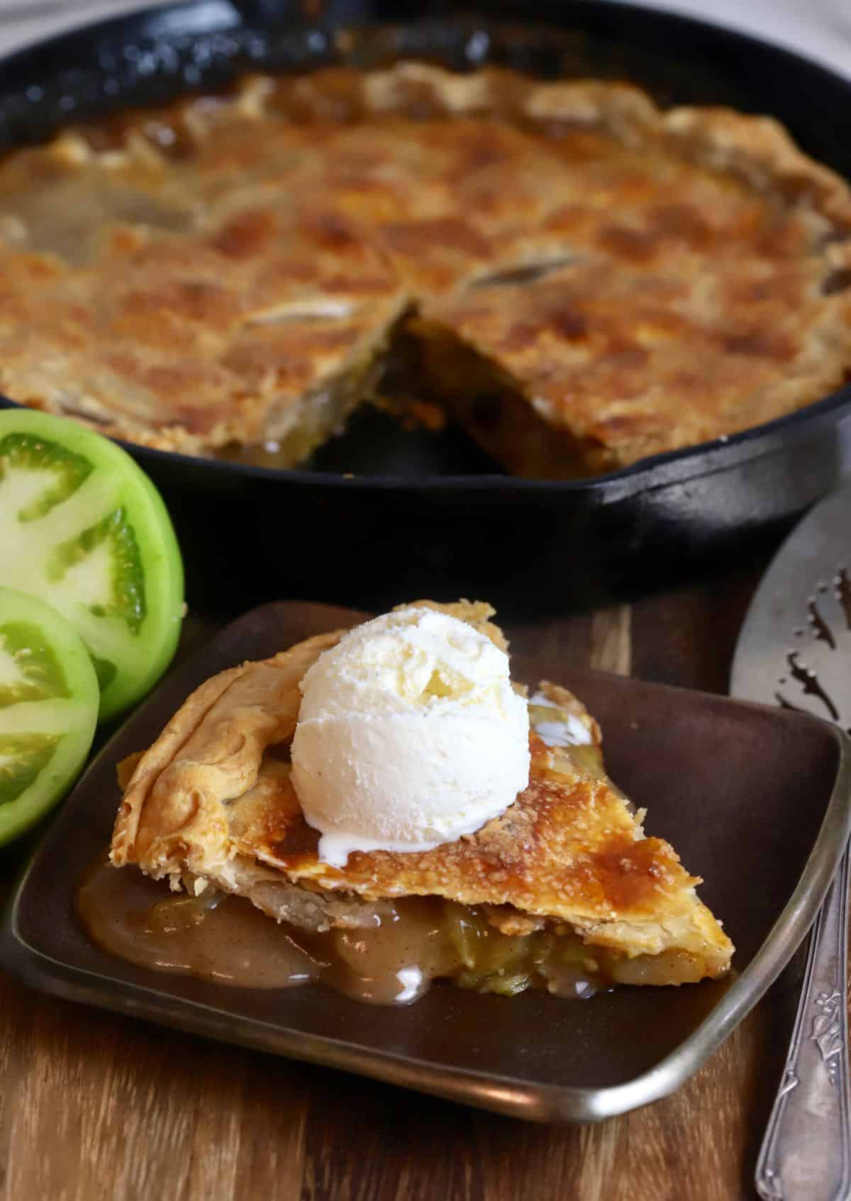 A cast-iron skillet with a slice of tomato pie cut out topped with a scoop of vanilla ice cream. 