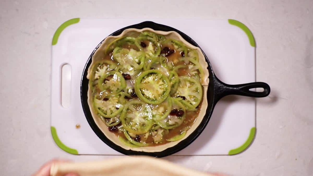 A cast-iron skillet with pie crust and tomato filling. 