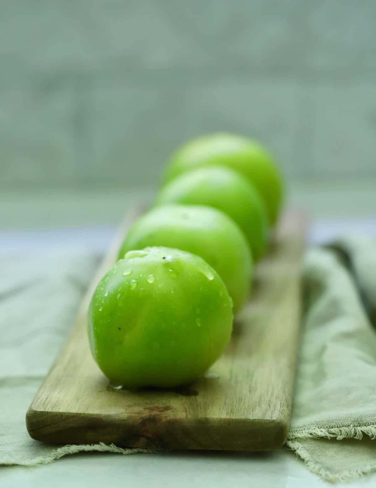 Four green tomatoes on a small cutting board. 