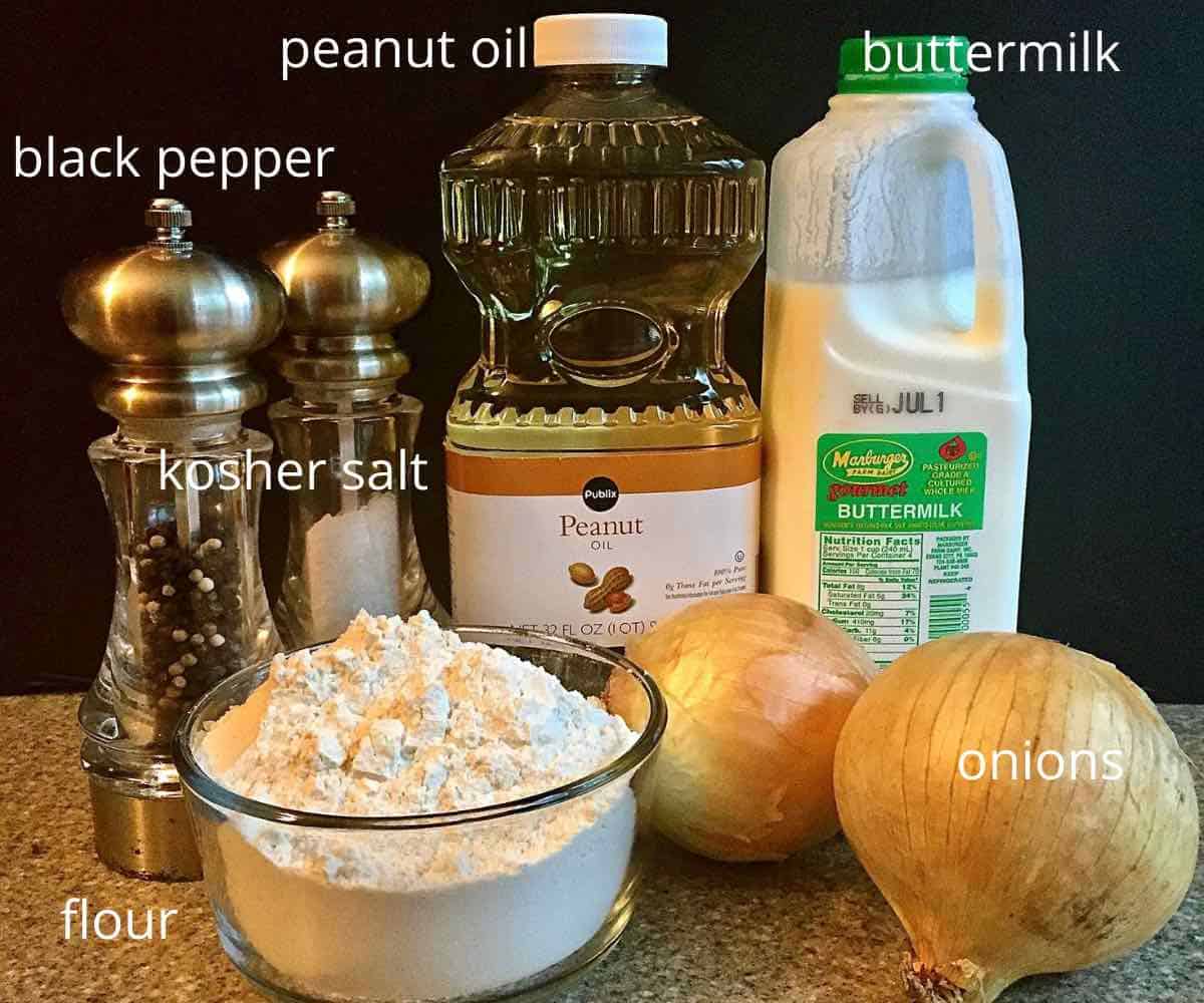 A bowl of flour, peanut oil, onions and buttermilk on a table.