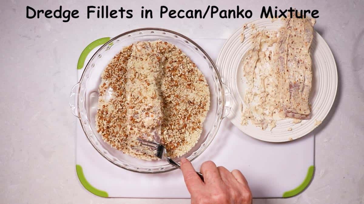 A fish fillet being dredged in a mixture of pecans and panko. 