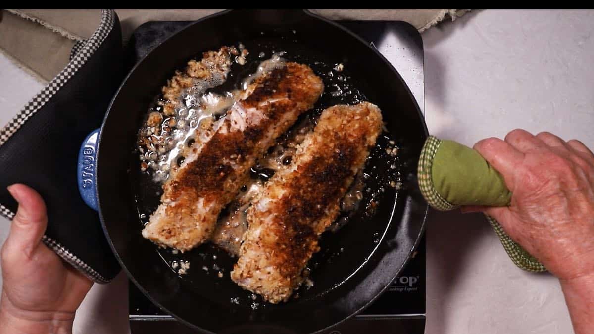 Two fish fillets cooking in a cast-iron skillet. 