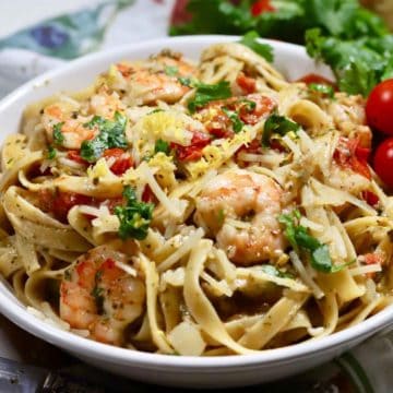 Pasta, pesto, shrimp and tomatoes in a large white bowl.