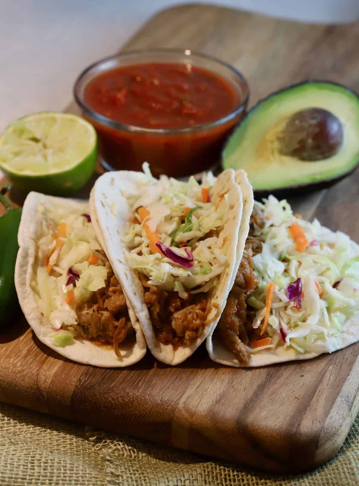 Three pork tacos on a wooden cutting board. 