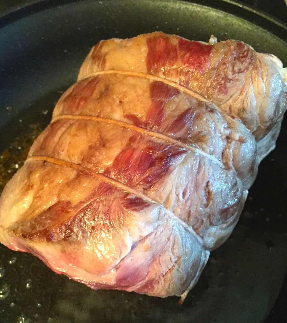 A pork roast cooking in a skillet. 