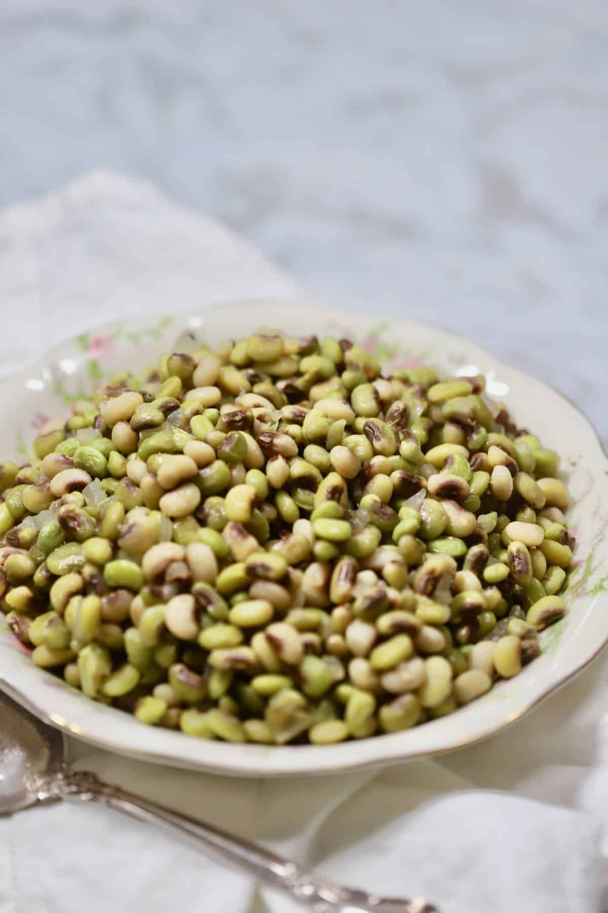 A bowl of cooked peas and a spoon on a white linen napkin.