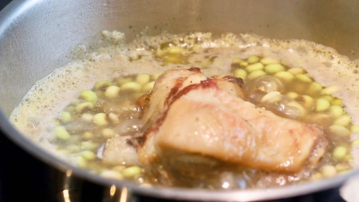 Peas cooking with a ham hock in a saucepan.