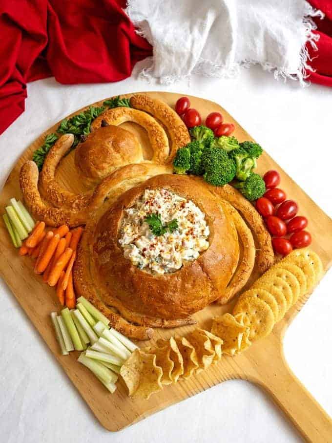 Bread shaped like a spider with dip and cut up veggies. 