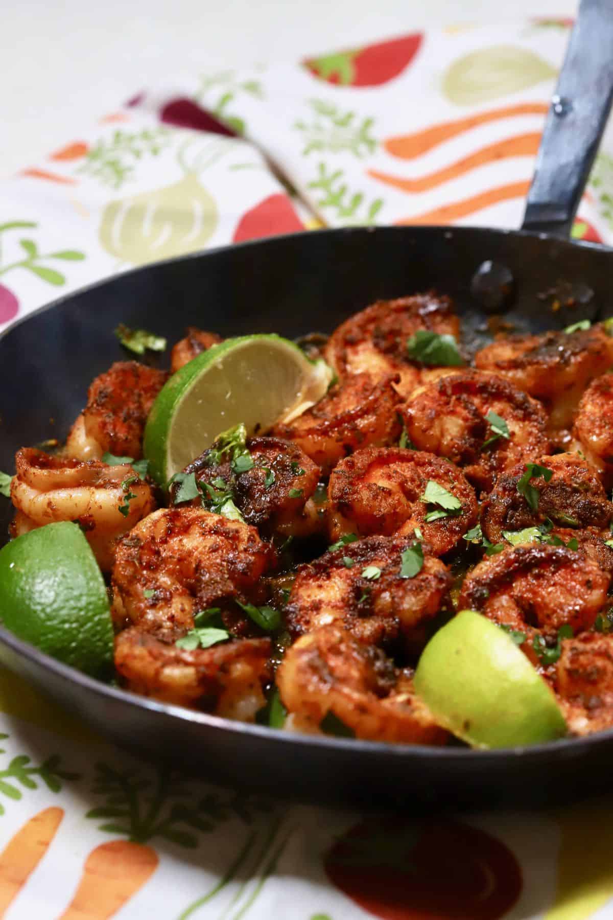 Blackened shrimp in a cast iron skillet garnished with lime wedges and parsley. 