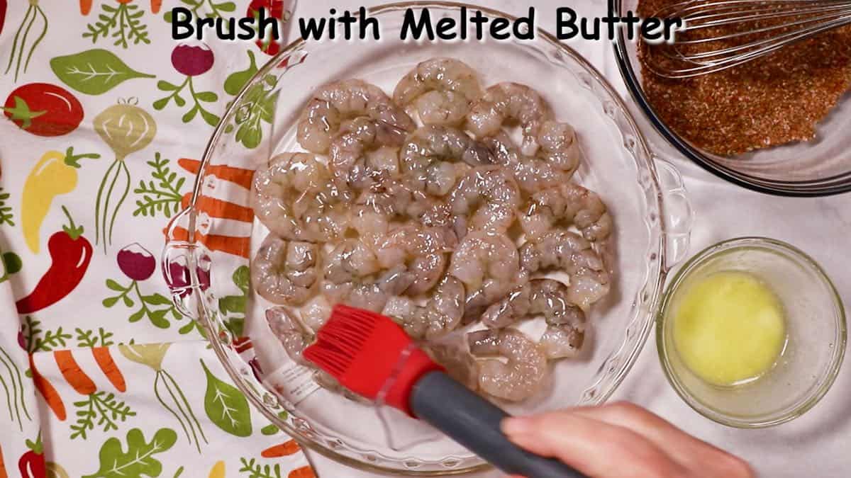 Brushing melted butter over shellfish in a dish.