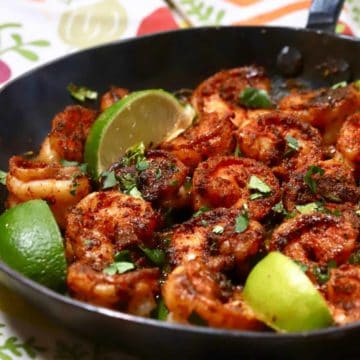 A cast-iron skillet full of blackened shrimp and garnished with lime slices.