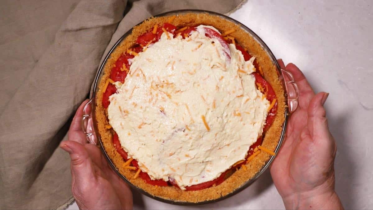 A tomato pie topped with parmesan cheese and mayonnaise mixture.