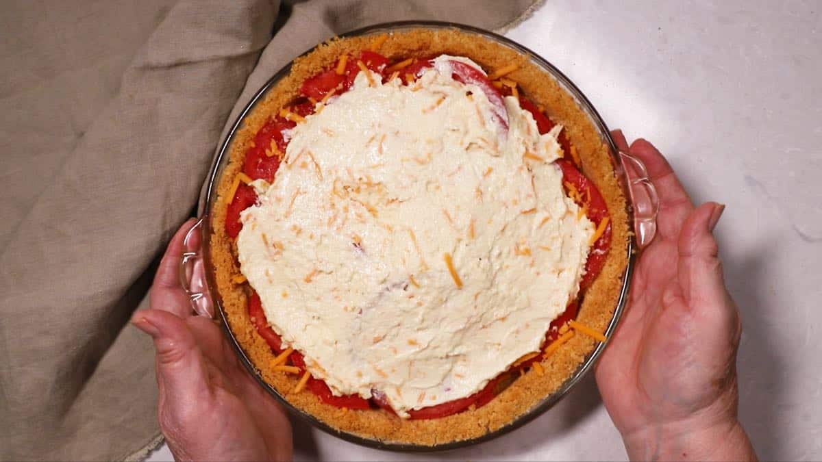 A tomato pie topped with parmesan cheese and mayonnaise mixture. 