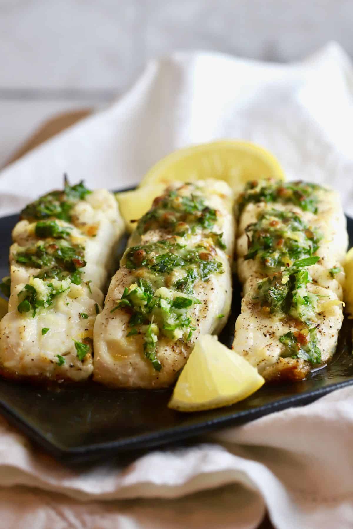 Three broiled halibut fillets on a black plate. 