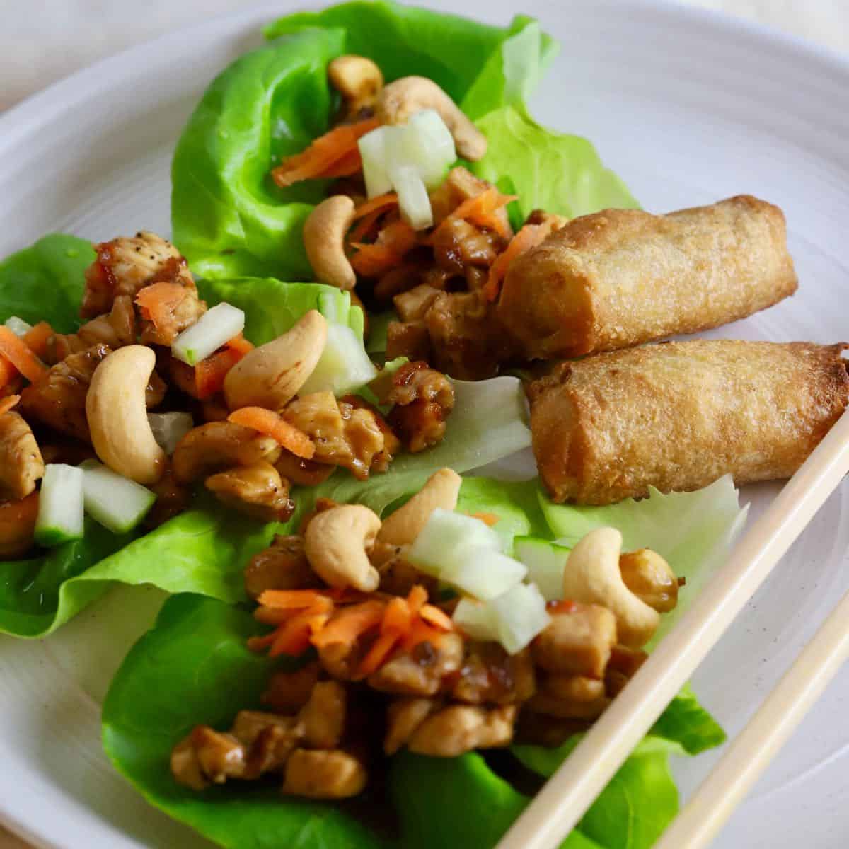 Three chicken lettuce wrap on a plate with spring rolls.