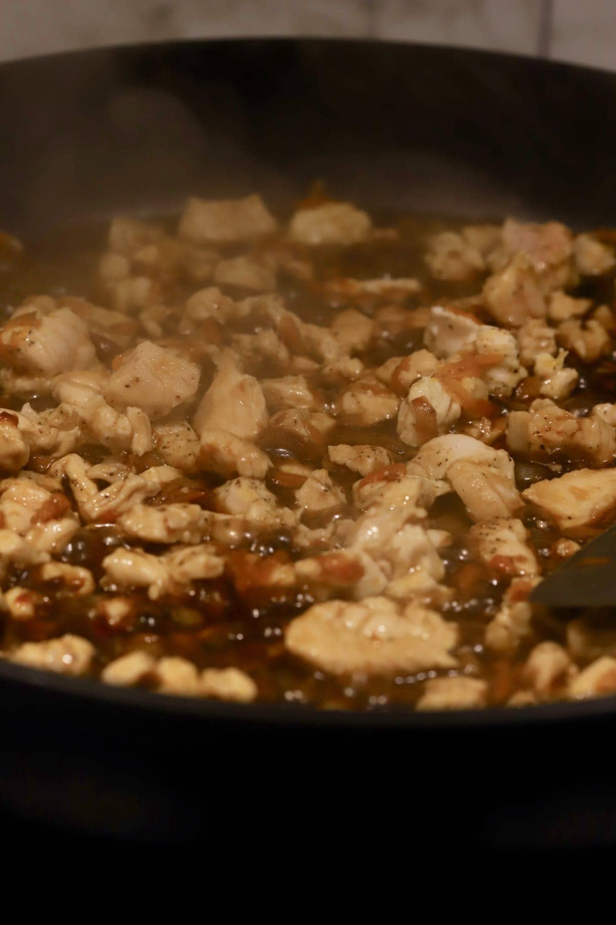 Chicken and sauce cooking in a skillet. 