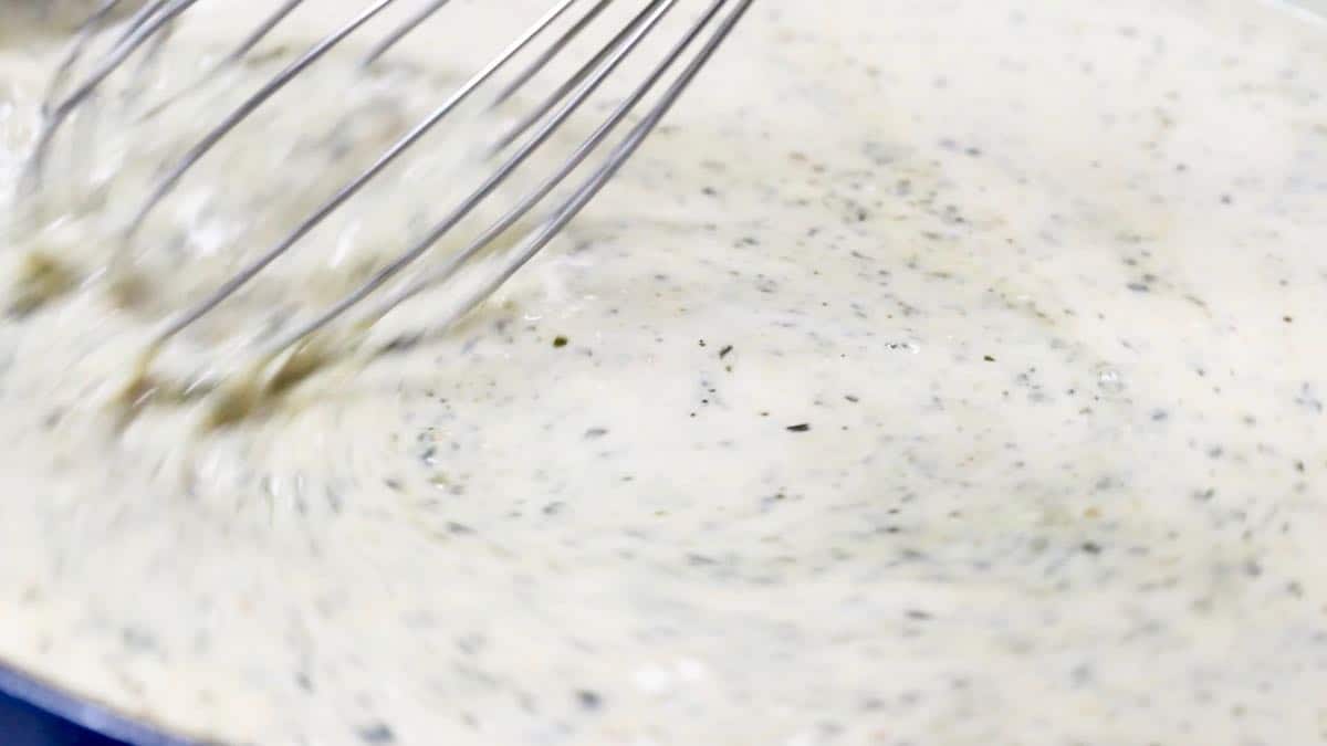 Using a shisk to stir alfredo sauce with pesto. 