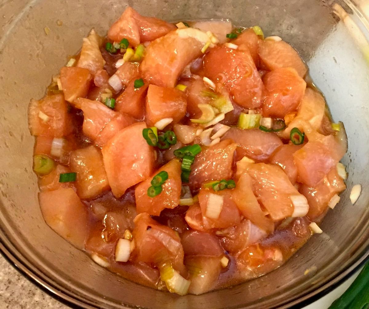 Pieces of chicken marinating in a glass bowl.