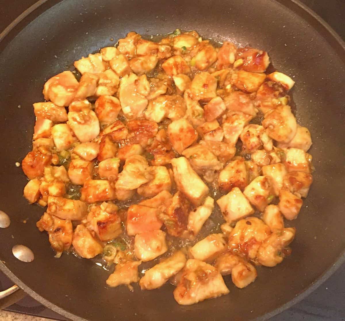 Small pieces of chicken cooking in a black skillet. 