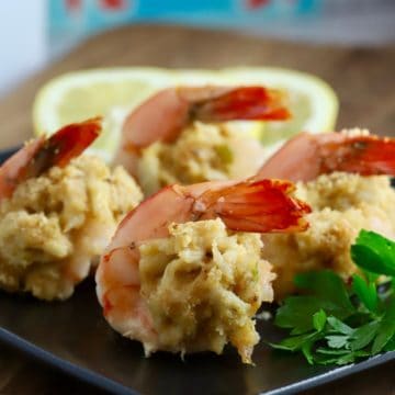 Crab stuffed shrimp on a black plate garnished with lemon slices.