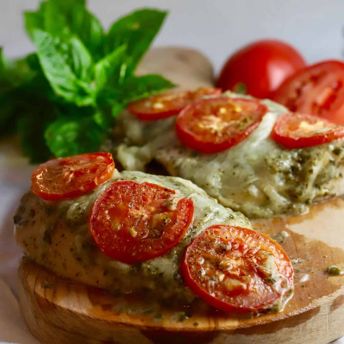 Two baked pesto chicken breasts topped with tomato slices.