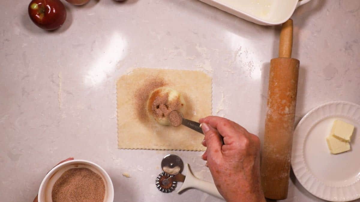 Sprinkling cinnamon sugar over an apple sitting on pastry dough. 