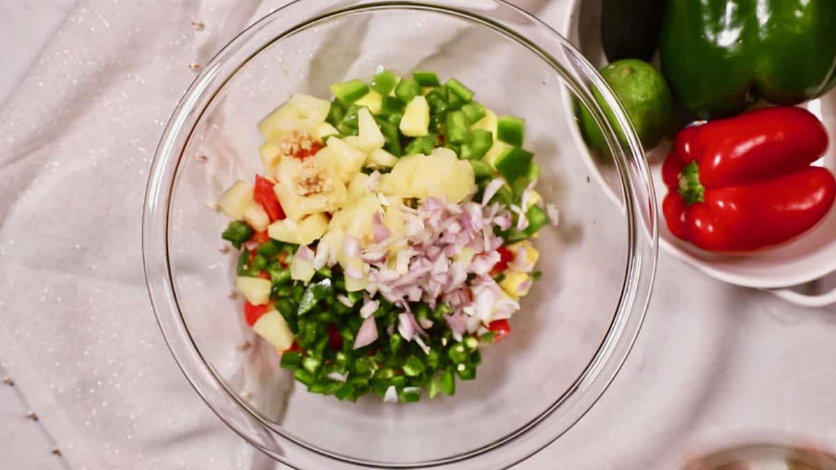 Mango salsa ingredients including mango and pineapple in a clear glass bowl. 