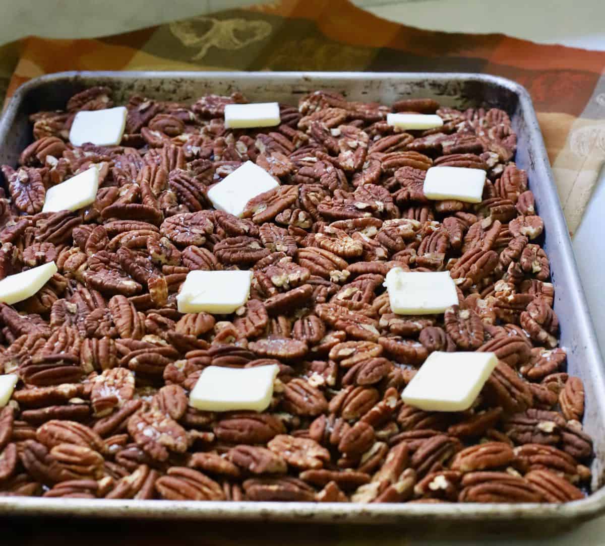 A baking sheet with pecans topped with pats of butter. 