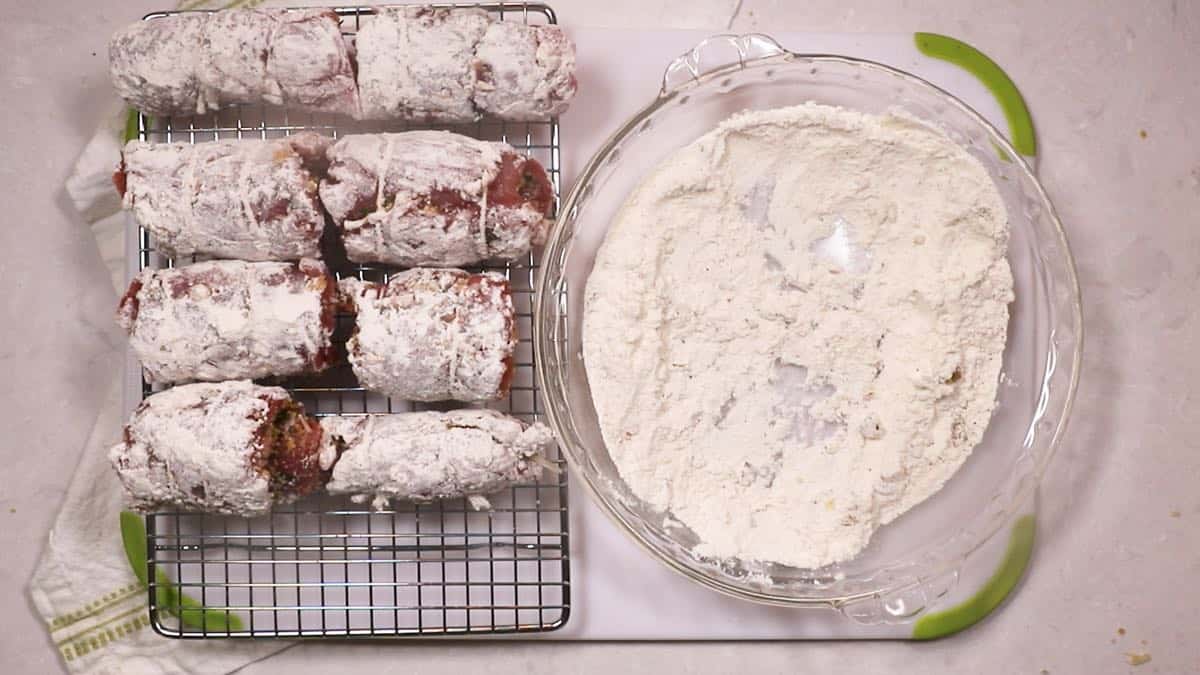 Eight stuffed pork rolls that have been dredged in flour. 