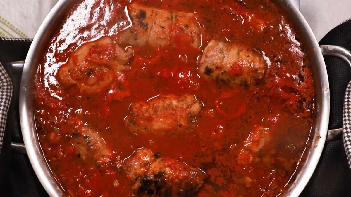 Pork braciole cooking in marinara sauce in a skillet. 
