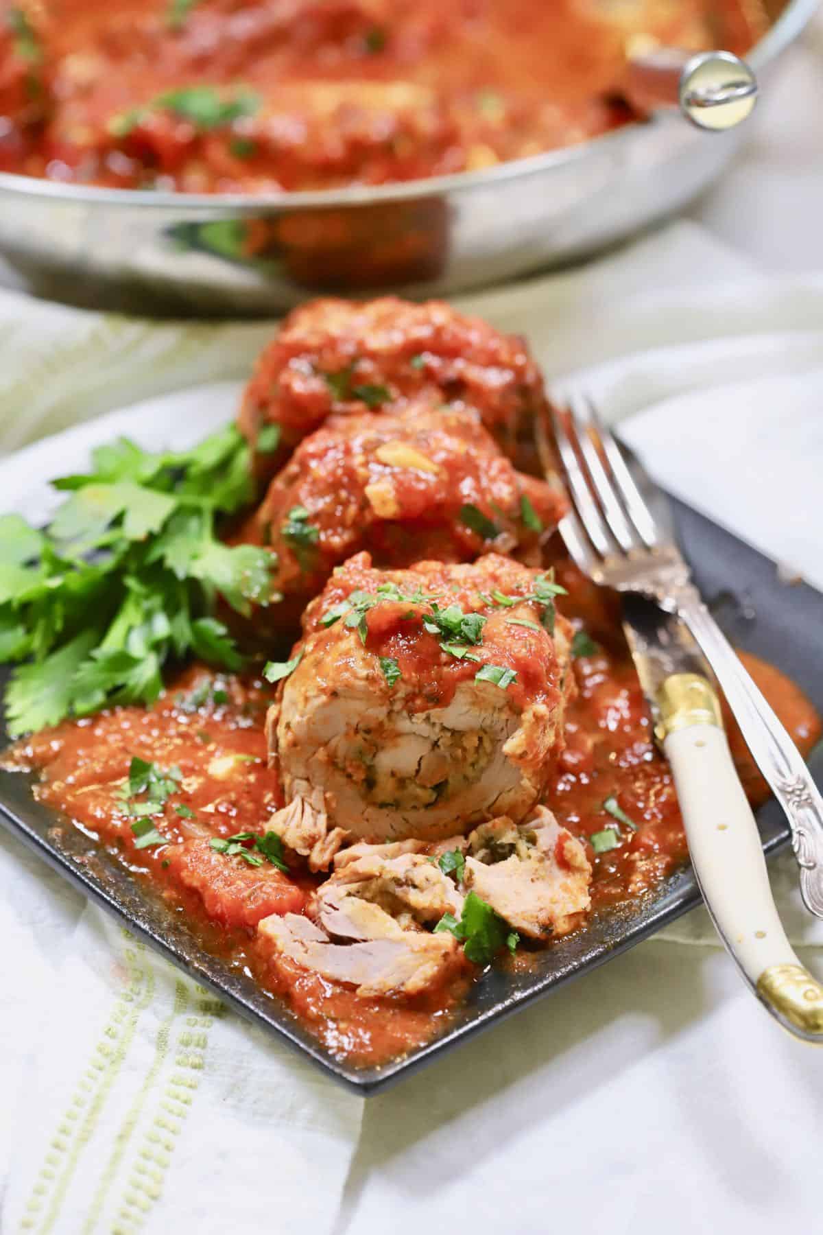 A plate of pork braciole with a knife and fork.