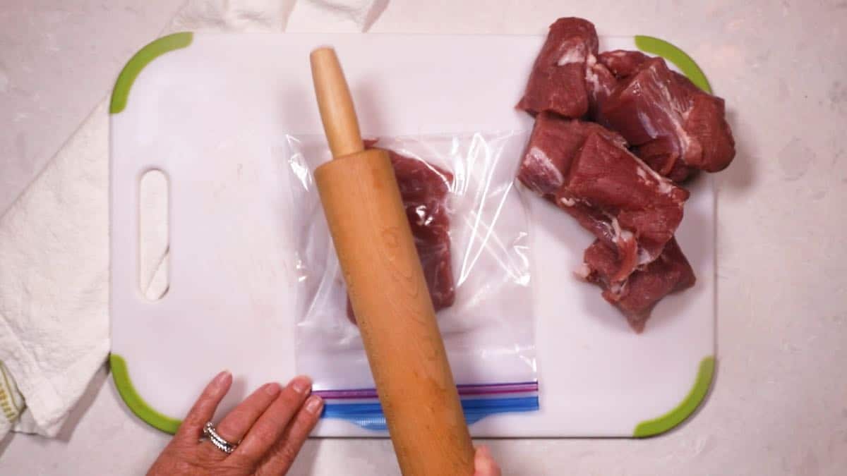 Using a rolling pin to pound a piece of meat thinner. 