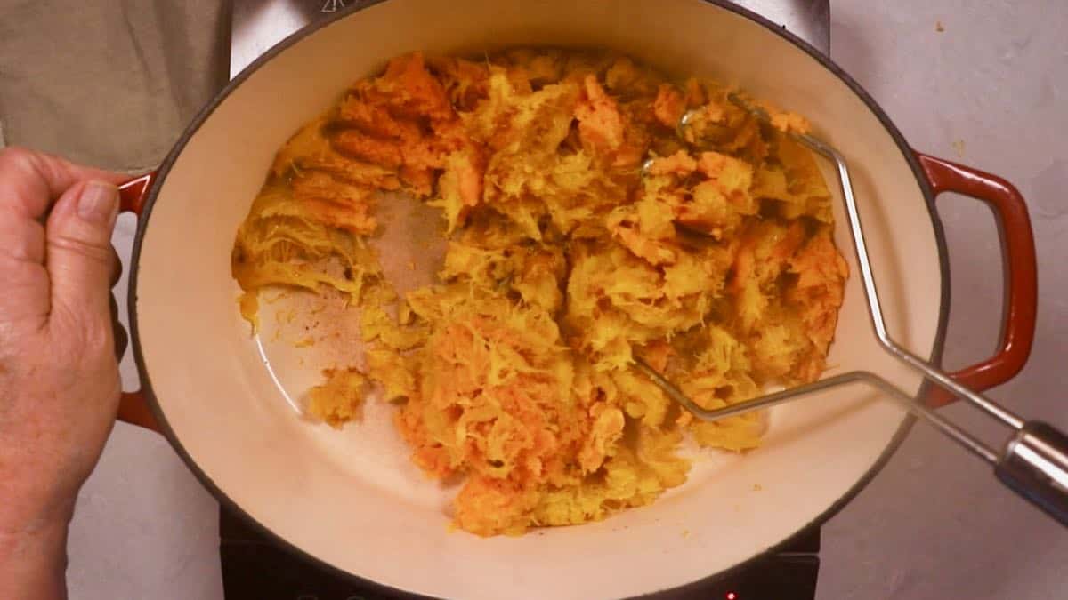 Using a potato masher to mash up cooked pumpkin. 