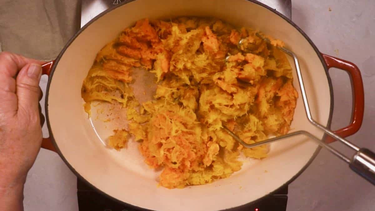 Using a potato masher to mash up cooked pumpkin. 