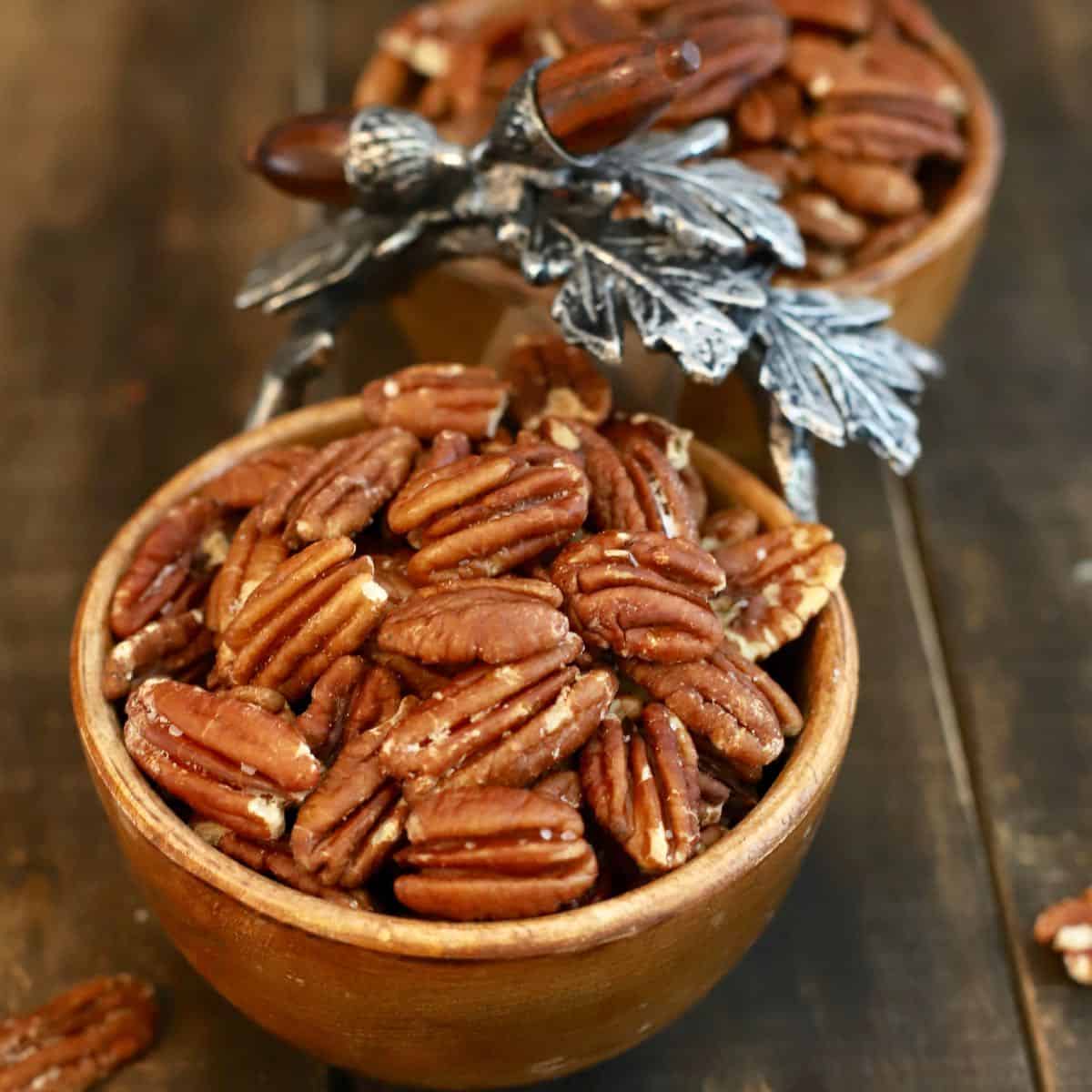 Toasted pecans in a wooden dish with pewter leaves.