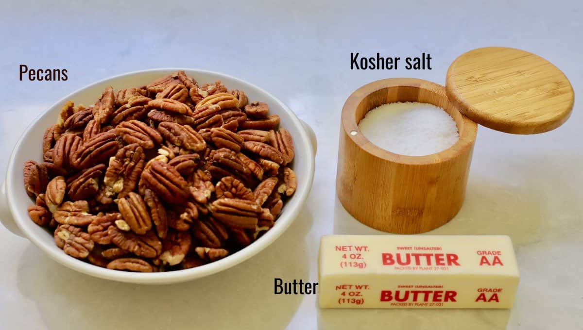A large bowl of pecans, kosher salt and butter on a kitchen counter.