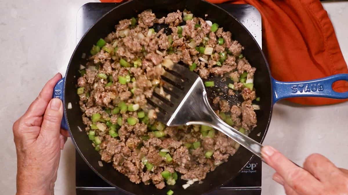 Sausage, chopped onions, and celery cooking in a skillet. 