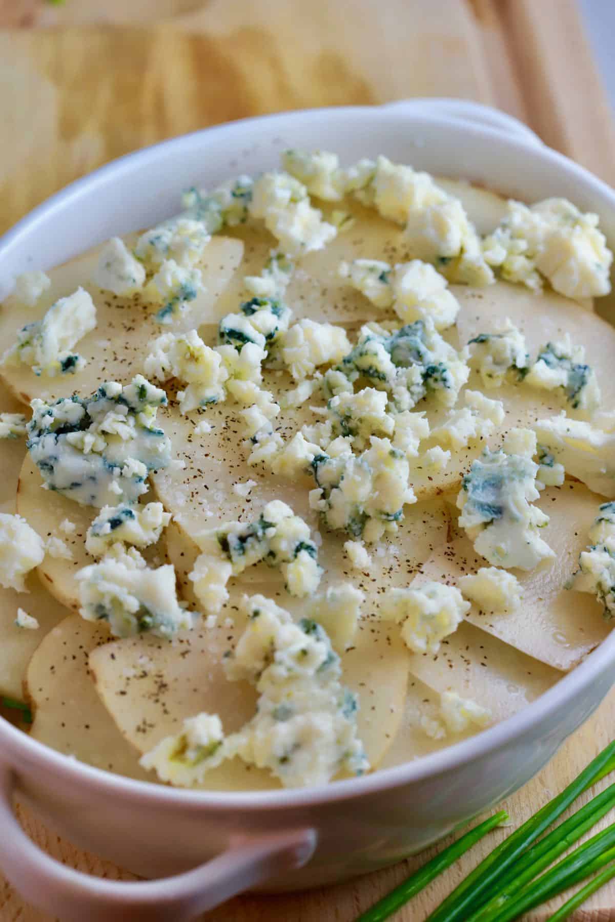 Sliced potatoes in a white baking dish topped with blue cheese. 