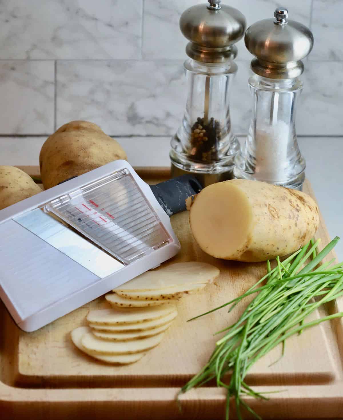 A mandoline with sliced potatoes on a cutting board. 