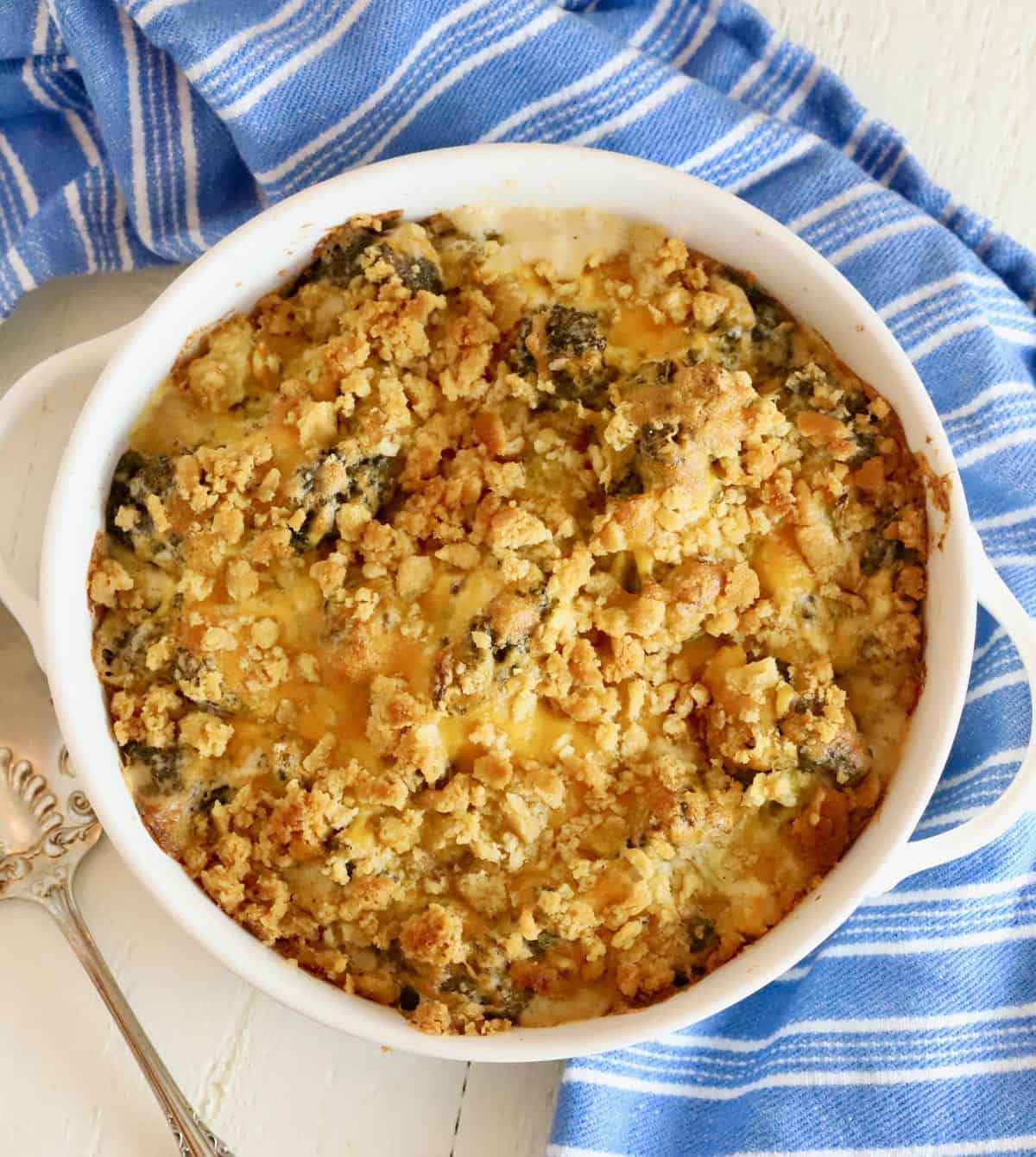 Broccoli cheese casserole in a white baking dish with a silver spoon. 