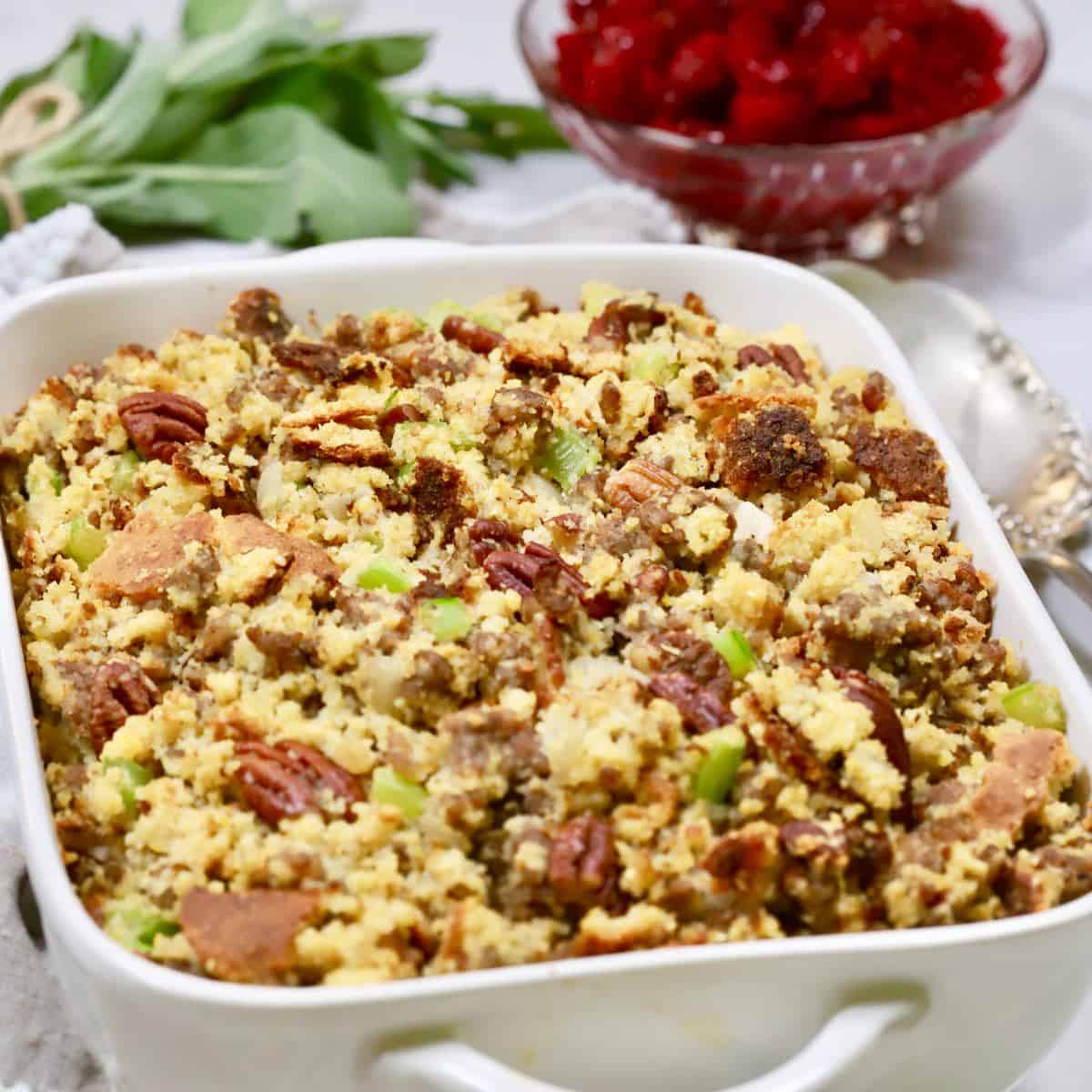 Cornbread dressing with sausage and pecans in a white serving dish.
