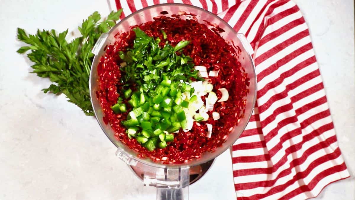A food processor with chopped cranberries, and jalapenos. 