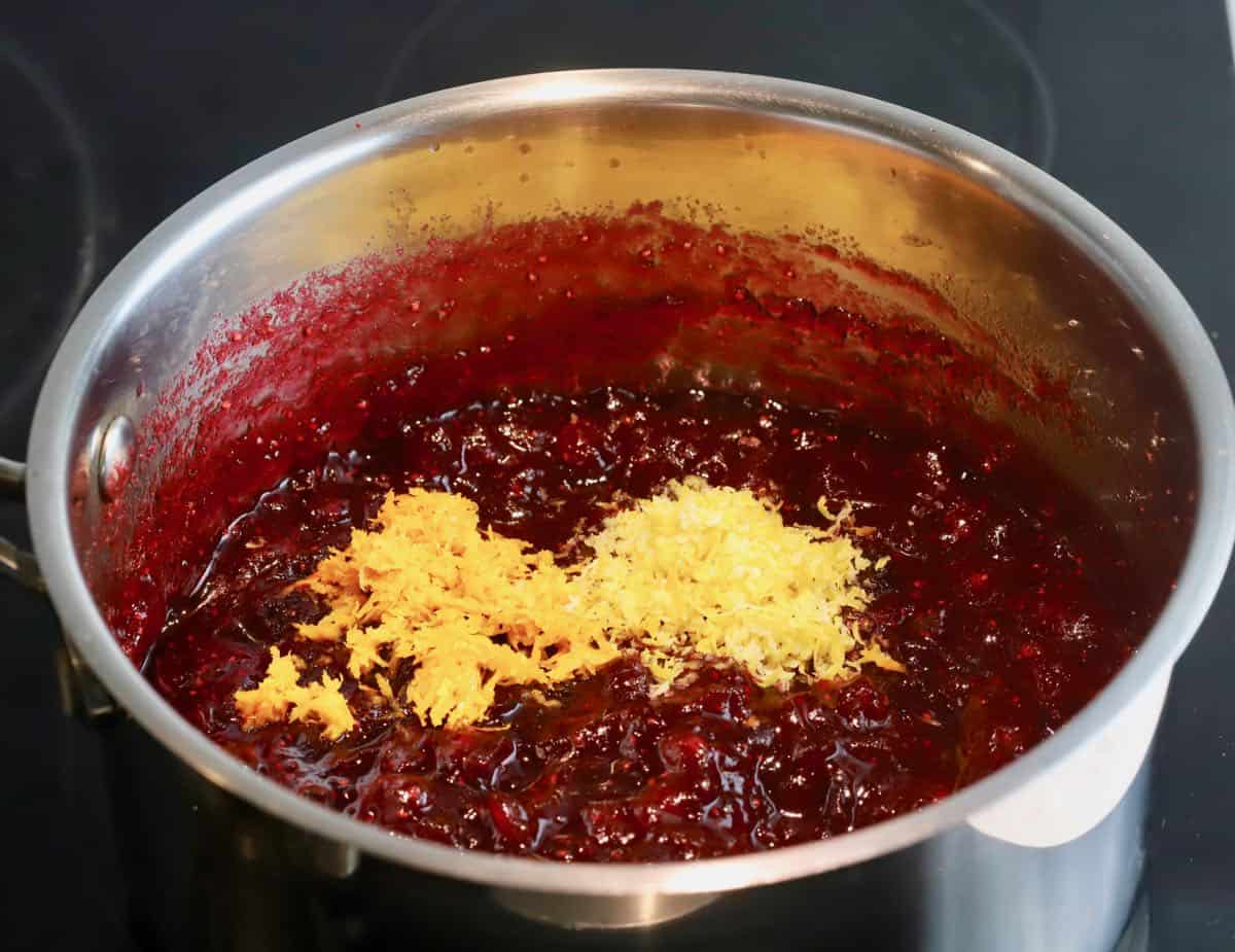 Orange and lemon zest added to cranberry sauce in a saucepan.