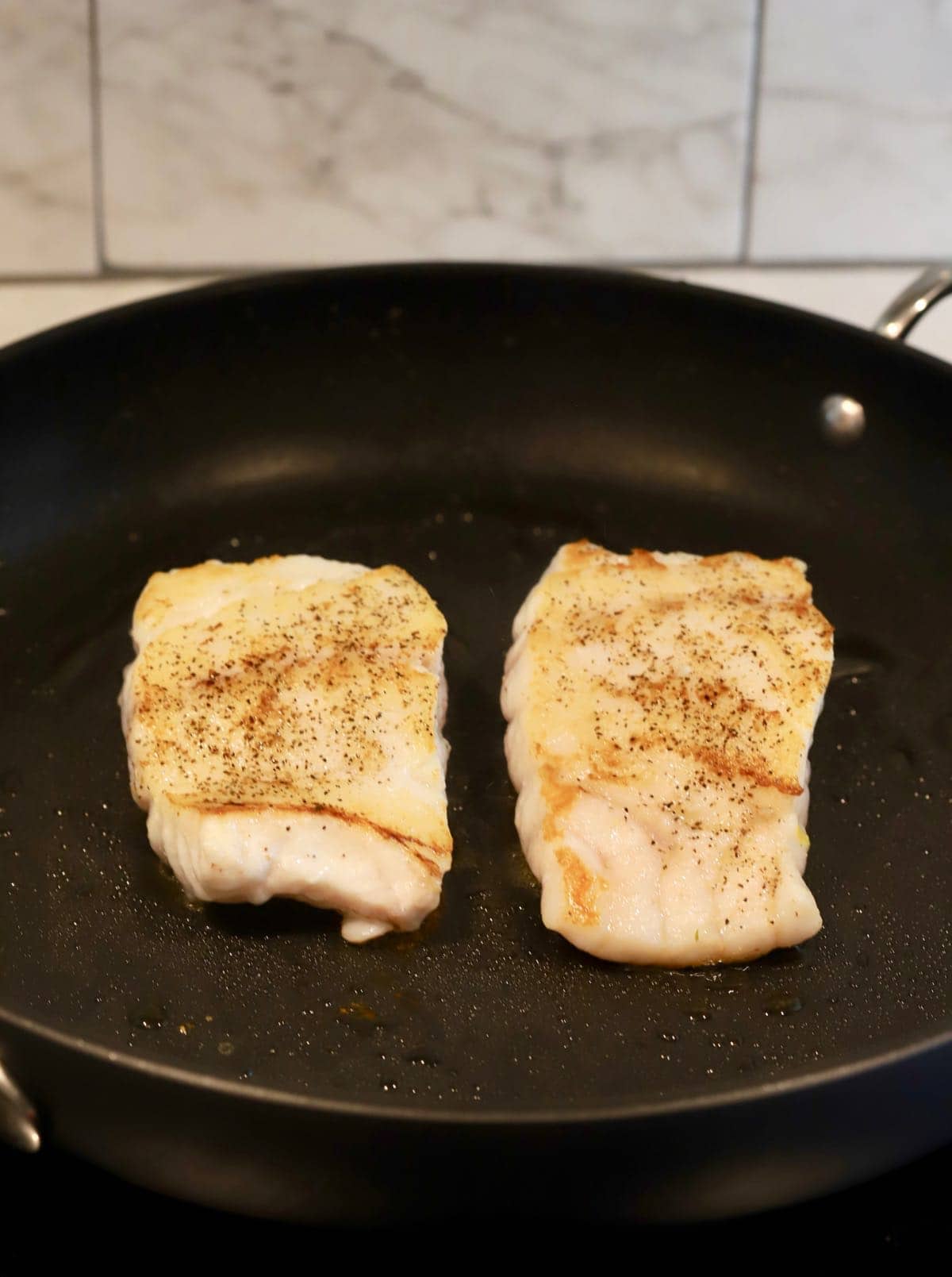 Two fillets of fish cooking in a skillet.