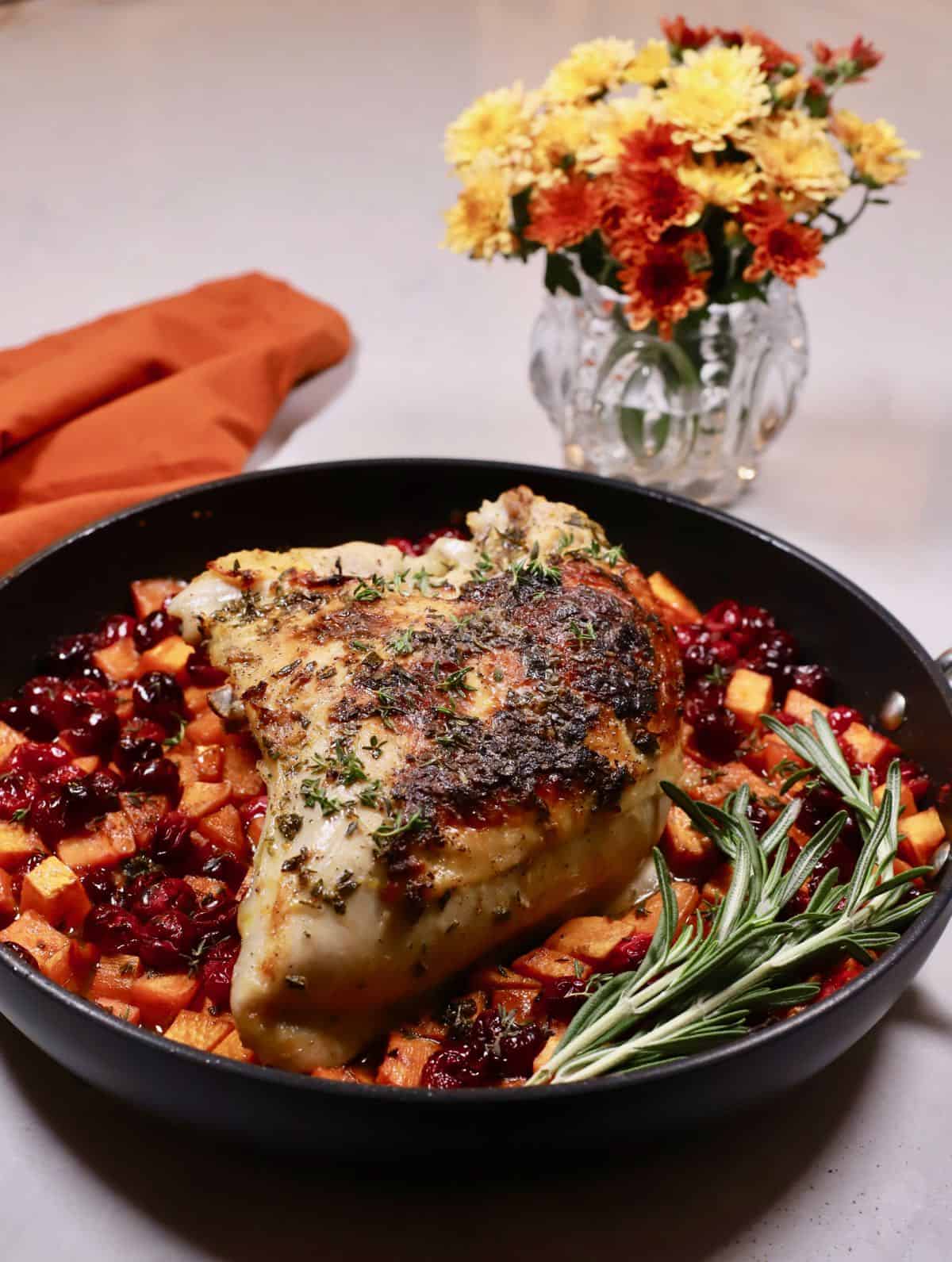 Roasted turkey breast in a skillet over sweet potatoes and cranberries.