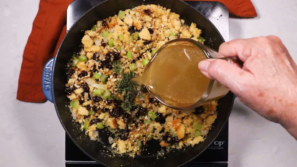 Adding chicken stock to cornbread dressing in a skillet.