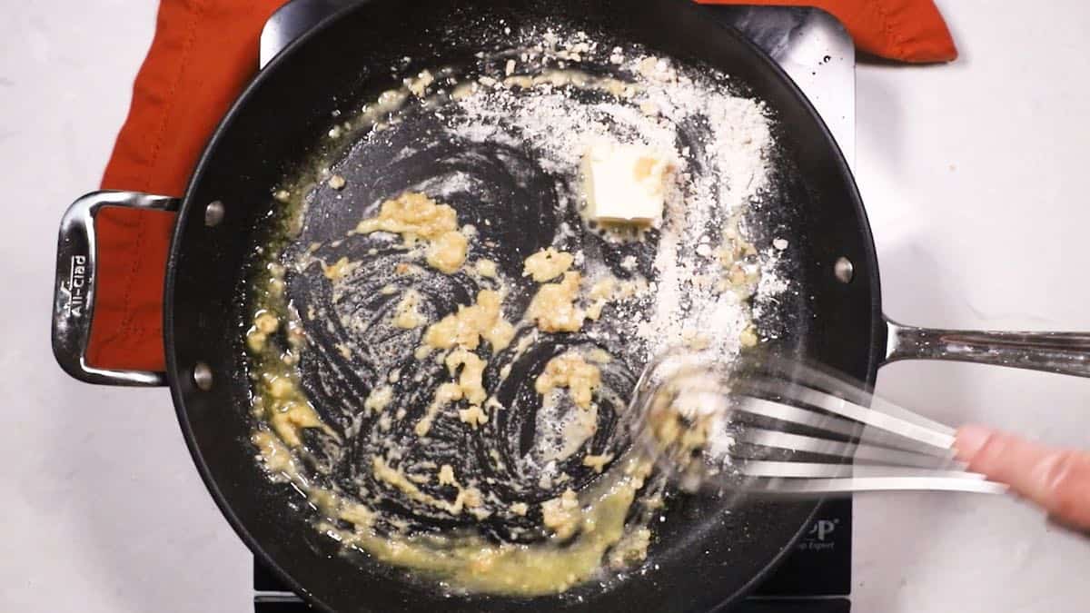 Whisking flour and butter together in a skillet.